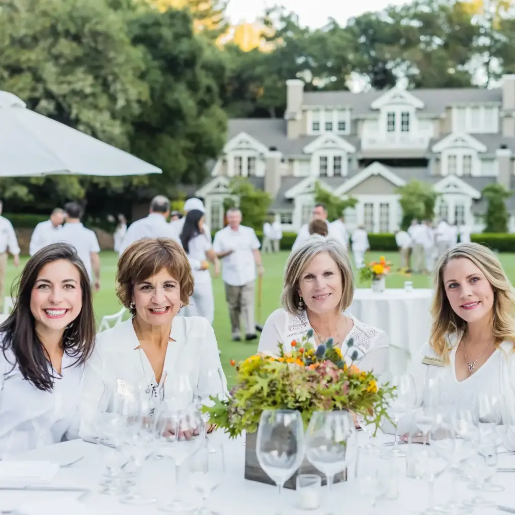 a group of women sitting at a table in front of a house.