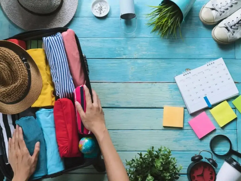a woman is putting clothes into a suitcase on a wooden table.