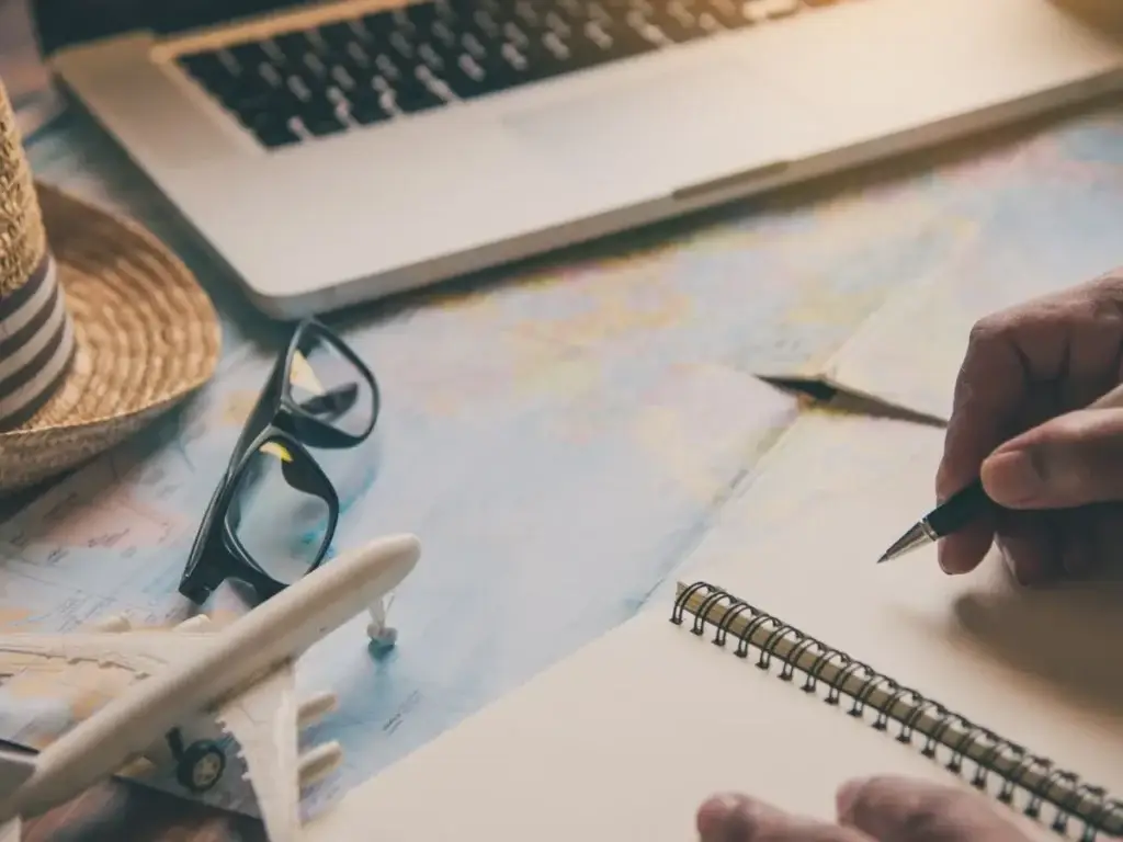 A man's hand writing on a notebook with a plane on it.