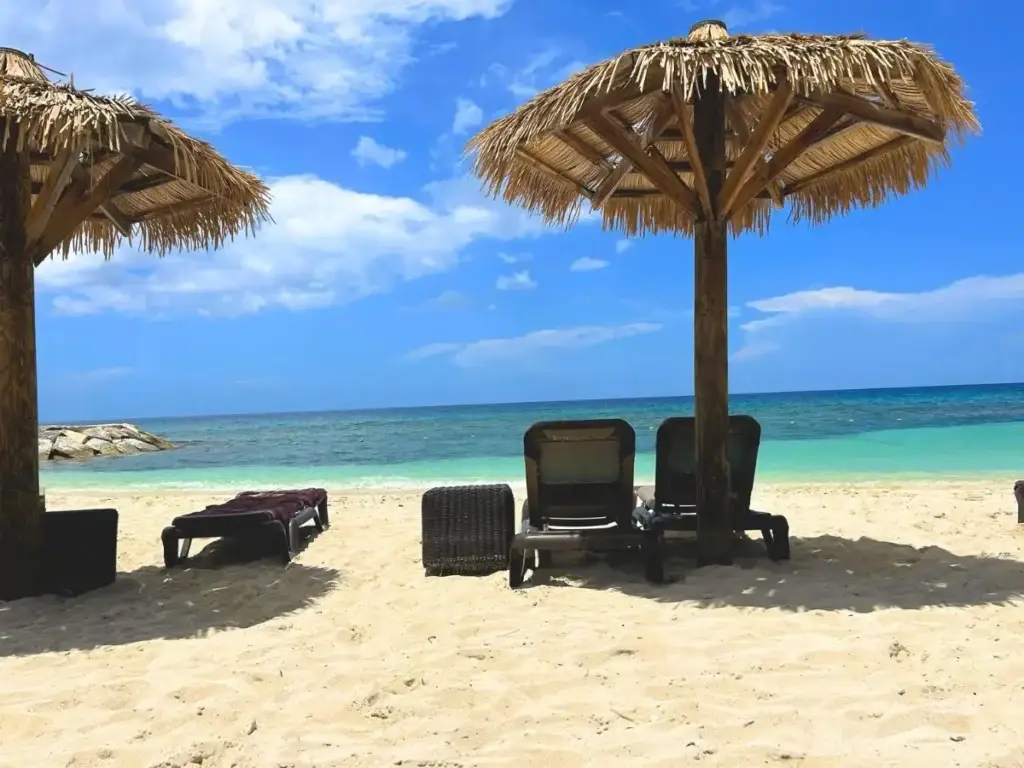 Three lounge chairs under thatched umbrellas on a sandy beach.