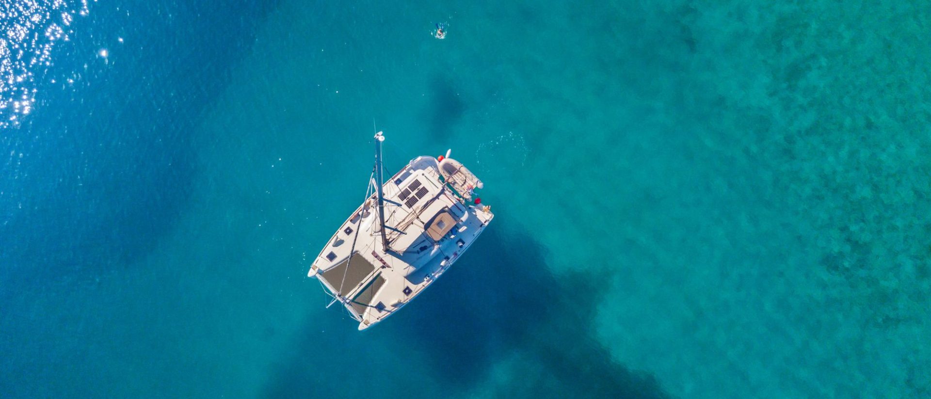An aerial view of a catamaran sailing in the clear blue water.