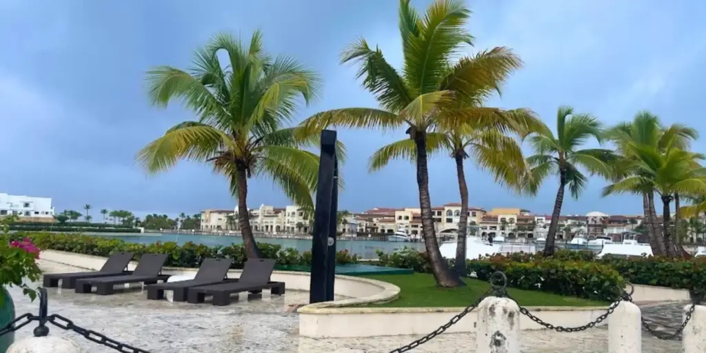 A picturesque walkway lined with majestic palm trees in Punta Cana, Dominican Republic. In the background, a serene boat gently floats on the crystal-clear turquoise water.